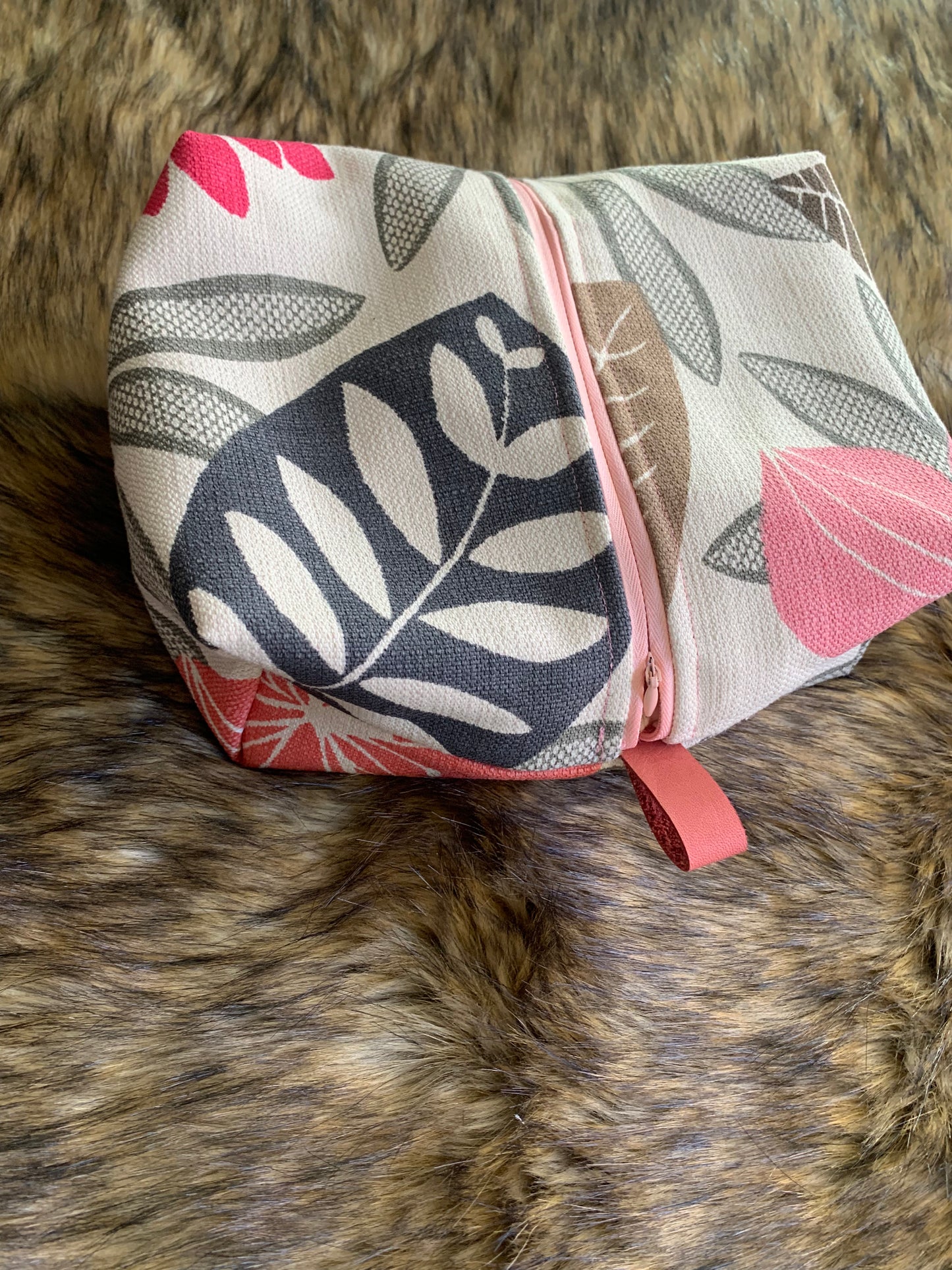 Travel cosmetic box bag in a large print stylized tropical floral greys and coral. Pink zipper and pink thumb handles. Zipper is centered vertically for larger opening. 100% cotton lining.